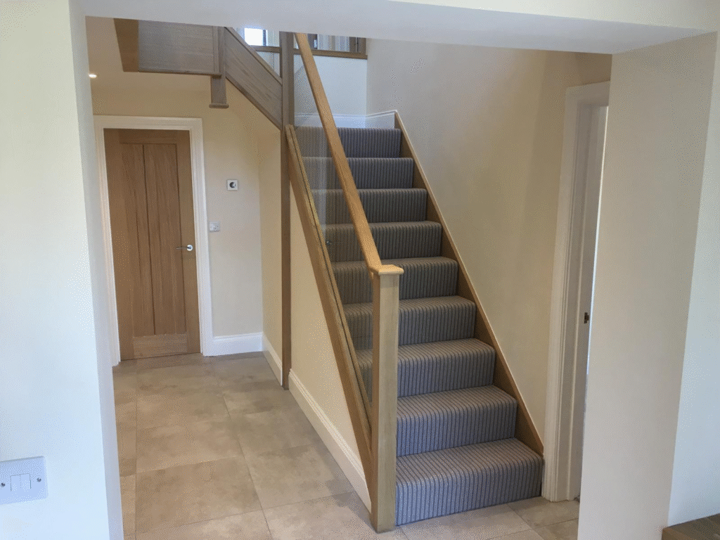Oak staircase with striped carpet runner and wooden handrail in a modern hallway