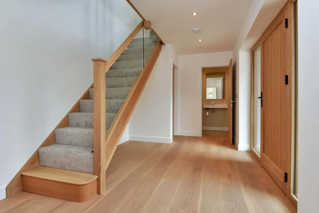 Modern hallway with oak staircase, glass balustrade, and light wooden flooring