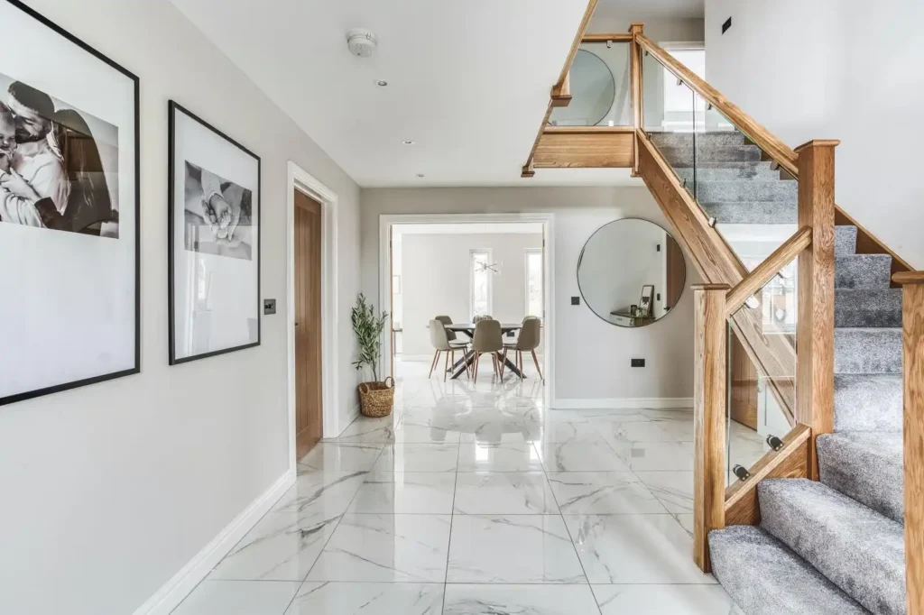 Stylish entrance hallway with glass staircase, marble floor tiles, and wall art décor